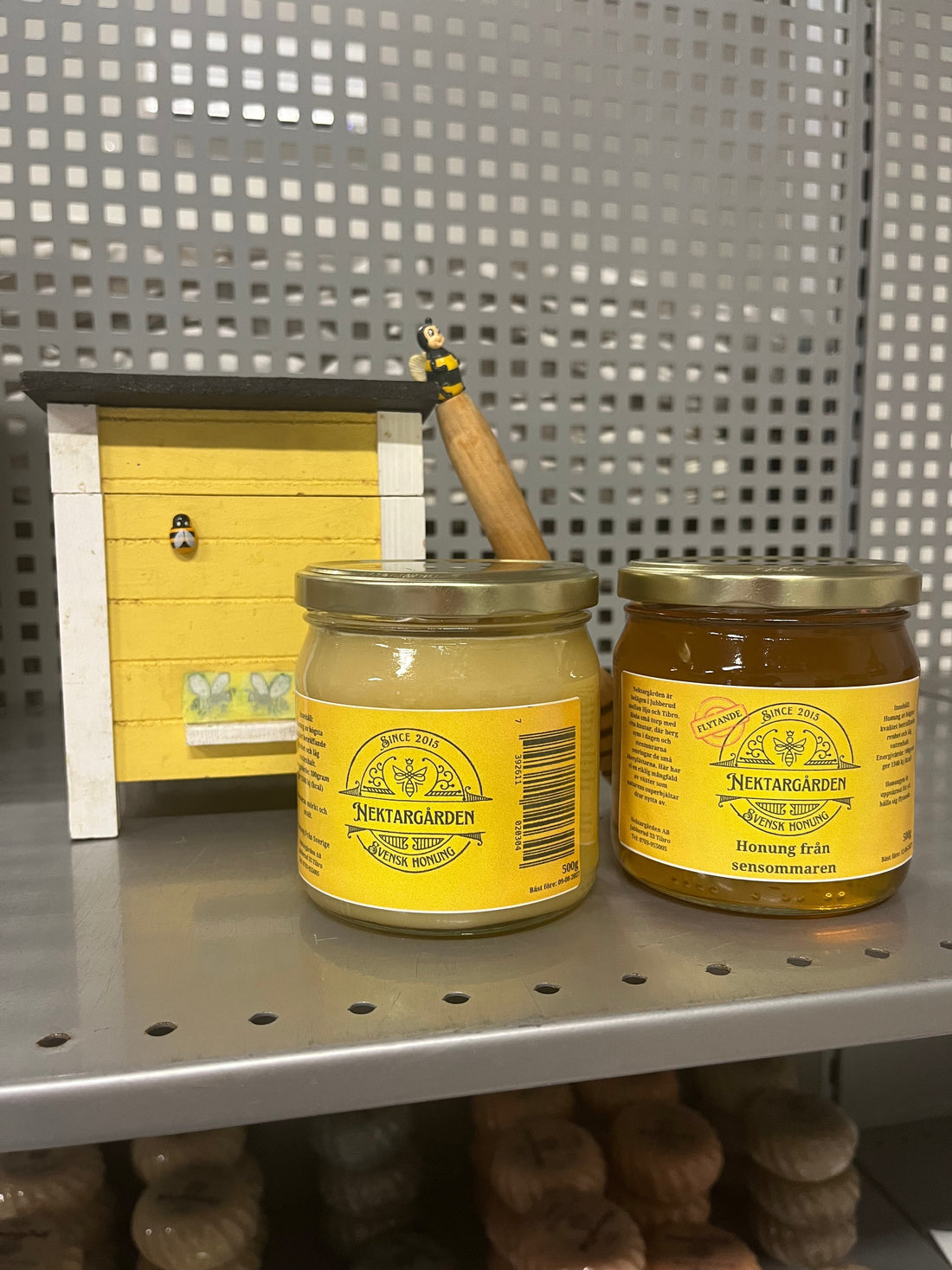 Flytande och klassisk honung på hylla med mini-bikupa och honungssked